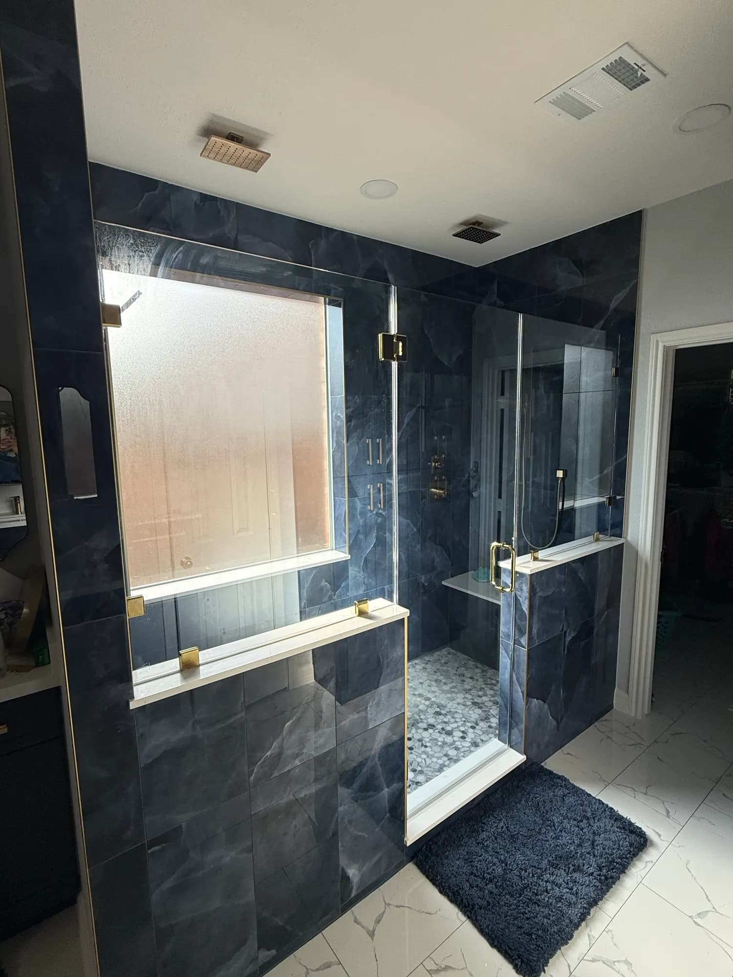 After: the same bath with a floor-to-ceiling navy stone-look tile shower, frameless glass, a bench and brass fixtures